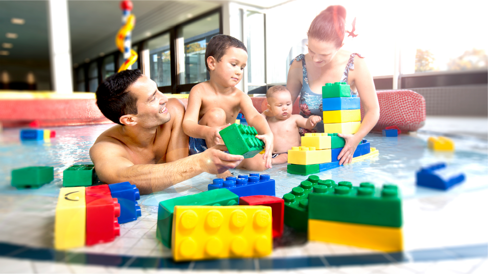 Familie aus Vater, Mutter und zwei kleinen Kindern in einem Becken im Hallenbad Böblingen. Die Familie spielt mit großen, bunten Bausteinen.