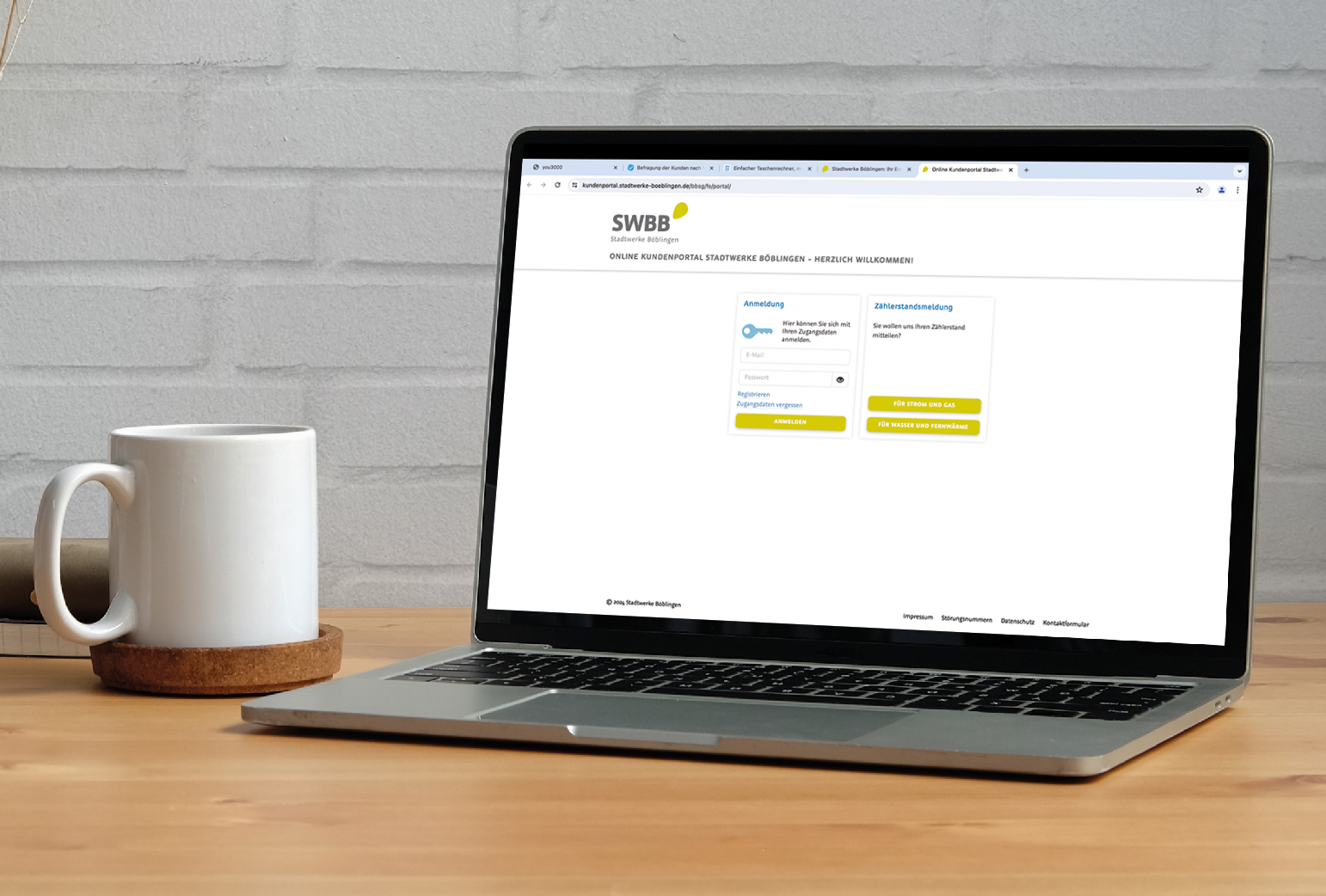 Digitales Kundenportal der SWBB: Bild eines Laptops neben einer weißen Tasse auf einem Holzschreibtisch. Auf dem Bildschirm ist das Kundenportal der SWBB Website geöffnet.