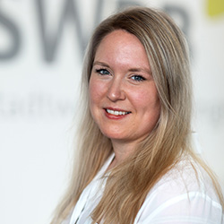 Caroline Jackson: Kommunikation der SWBB. Portrait einer lächelnden Frau mit langen blonden Haaren und weißem Hemd.