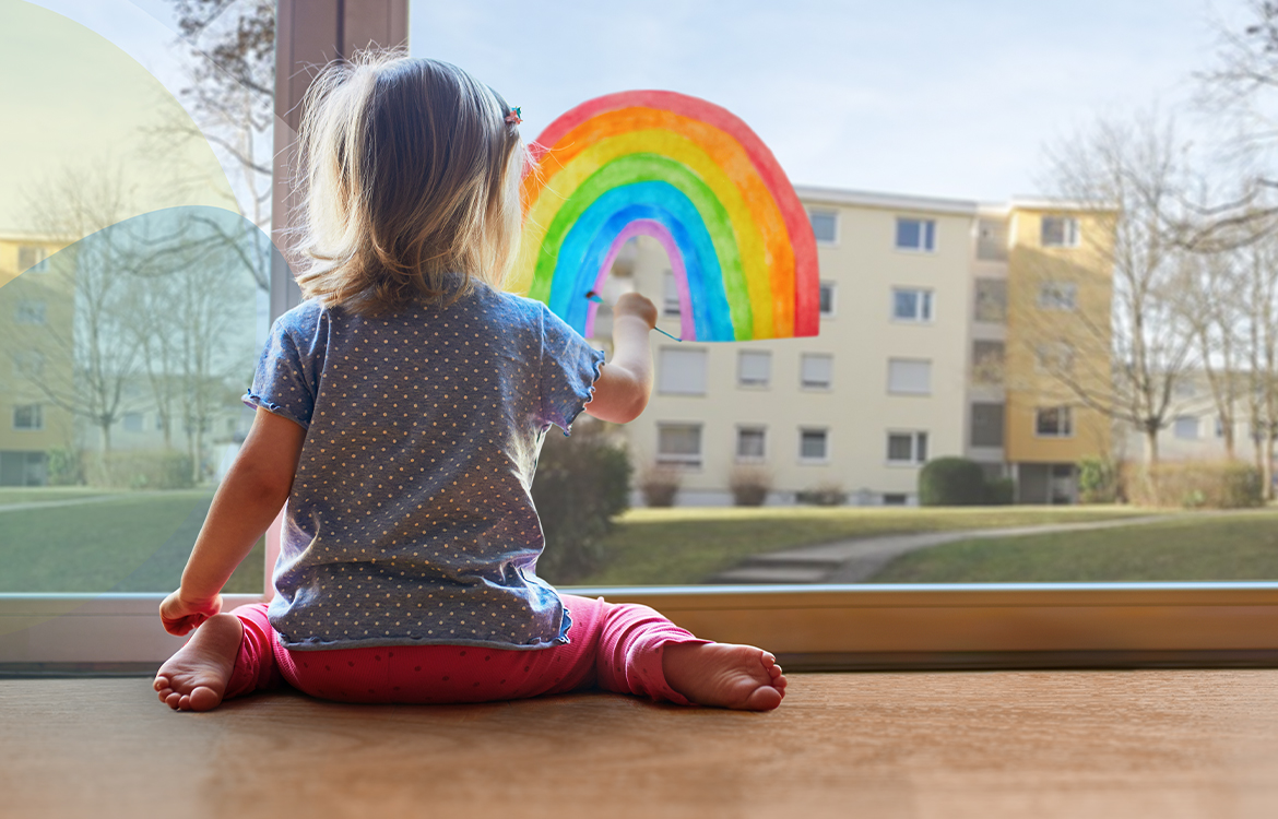 Kleines Kind auf warmem Fußboden durch Fernwärme in Böblingen. Malt einen Regenbogen an ein Terassenfenster. Hinter ihr bunte SWBB Sphären.